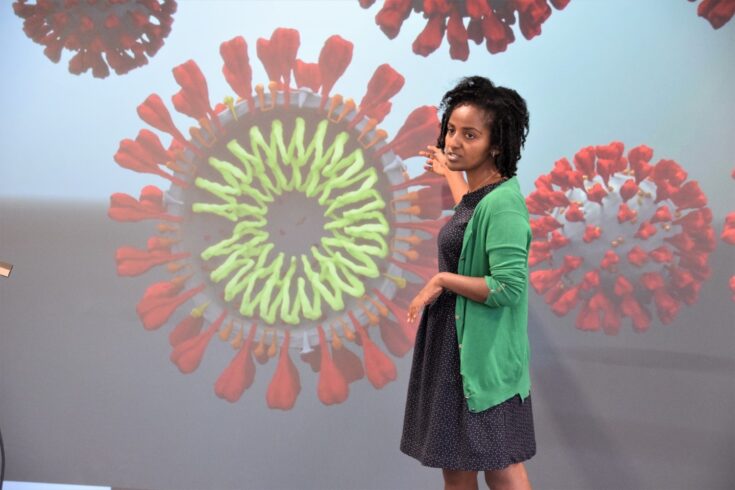 Woman presenting in front of a screen showing a virus