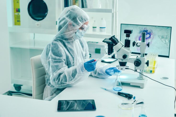 Scientist wearing PPE sat at a microscope