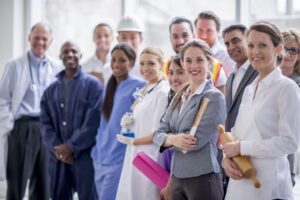 A multi-ethnic group of varied business professionals are standing together and are smiling while looking at the camera.