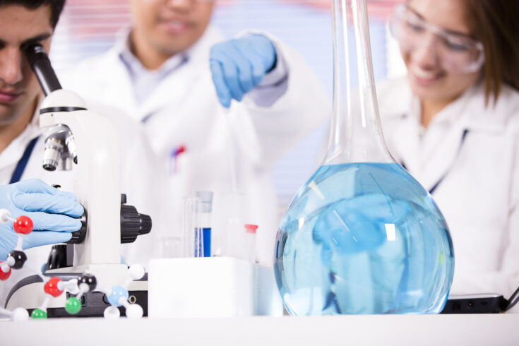 Multi-ethnic group of scientists working inside a research laboratory. They are conducting science experiments using test tubes, beakers, a microscope and chemicals.