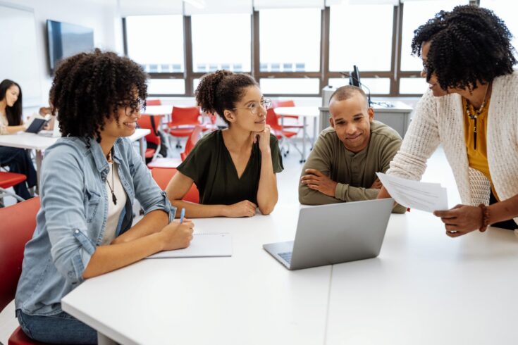 University students in modern classroom with lecturer. Students talking to female African professor during or after the lectures