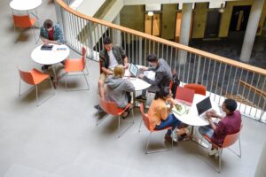 A group of students sitting at tables using laptops in a open plan space