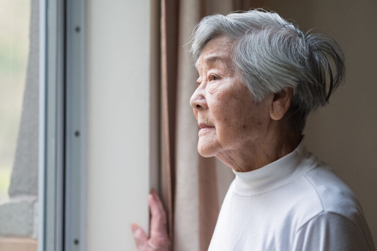 Serious Asian senior woman in 90s looking out of the window.