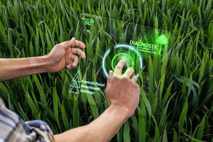 An unrecognisable farmer using an artificial intelligence tablet to scan his wheat crop in a field, he is able to carry out product analysis, quality assessment, statistics and the needs of the plant. He is clicking on the bug icon on the screen to check the soil moisture and ph levels.