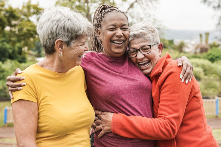 Happy multiracial senior women having fun together outdoor. Elderly generation people hugging each other at park.