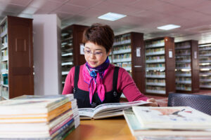 A female teacher in the library sitting at a table looking at books.