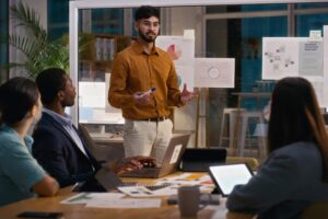 Creative business people, night and man in presentation for meeting, ideas or strategy at office. Staff, speaking or group of designers talking in team collaboration or sharing startup data analytics.