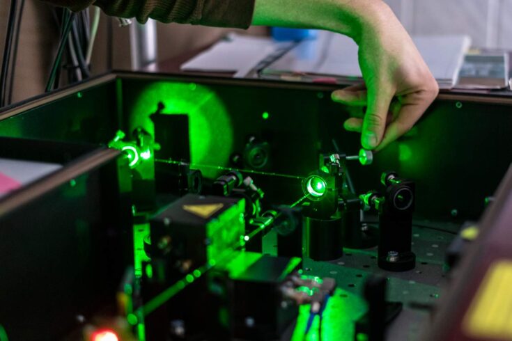 scientist working with laser machine or system, green lasers shooting across.
