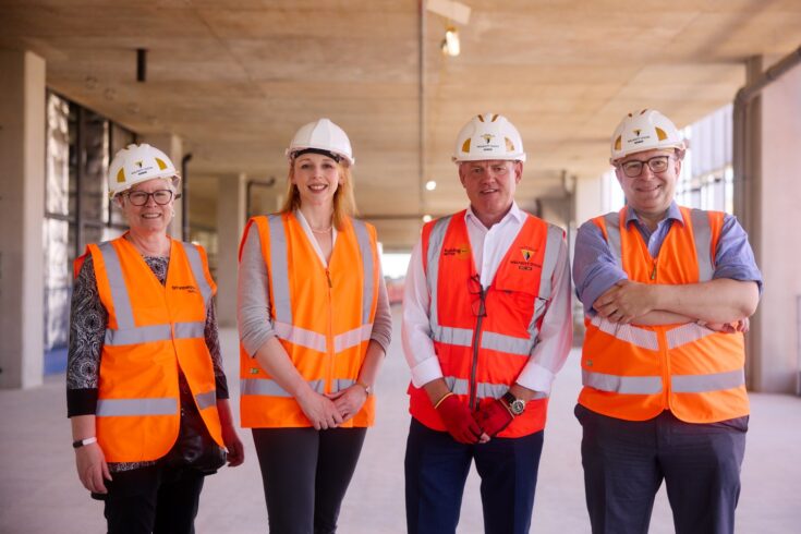 Four people wearing hi-ves zip gilets and safety helmets standing and smiling