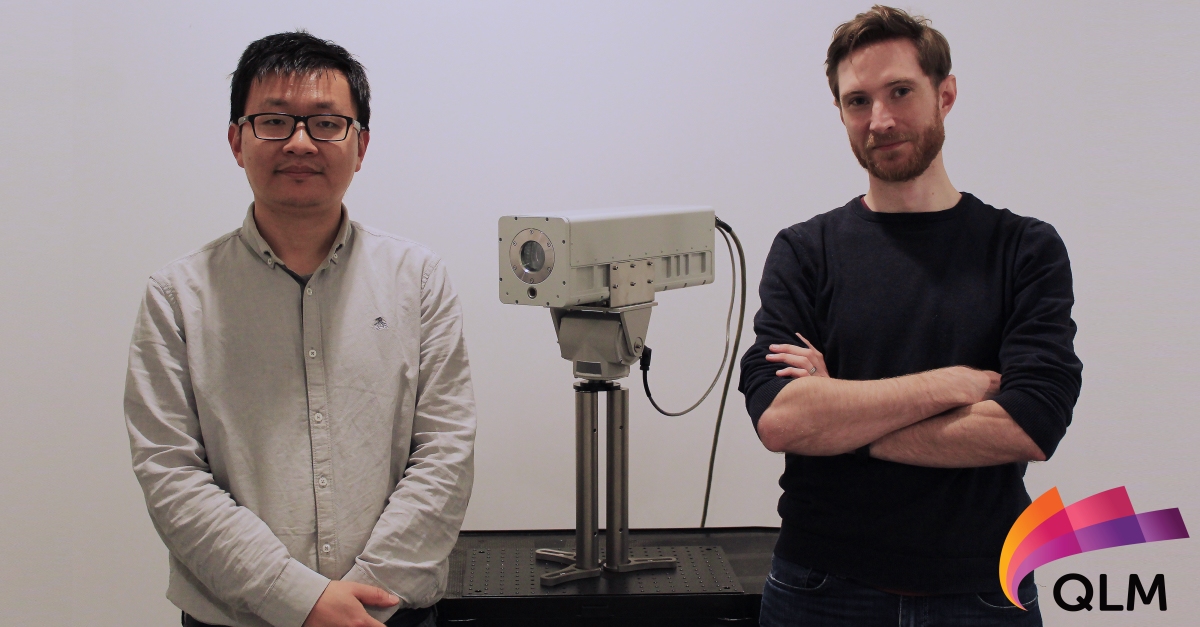 Two people standing between a gas imaging camera and smiling
