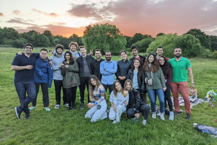 Group of people in a field with the sun setting in the background behind a backdrop of trees