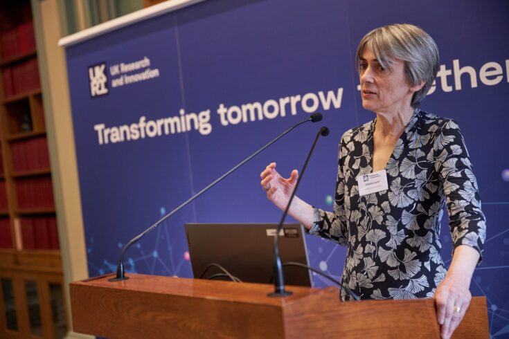 Professor Dame Ottoline Leyser speaking at an event, with the words 'transforming tomorrow' visible on a banner behind her.