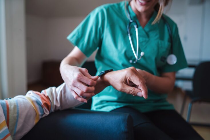 Nurse adjusting medical smart watch on persons arm.
