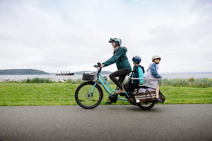 Mother riding an e-cargo bike with her children as passengers.