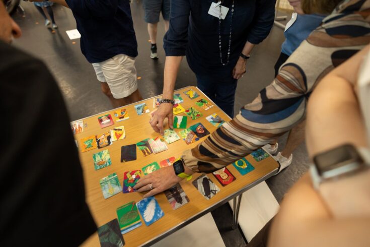 People reaching out to colourful cards on a wooden table that depict a range of faces and objects.