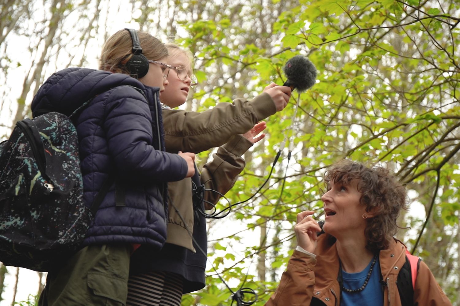 Two children using sound technology in a woodland area with their teacher.
