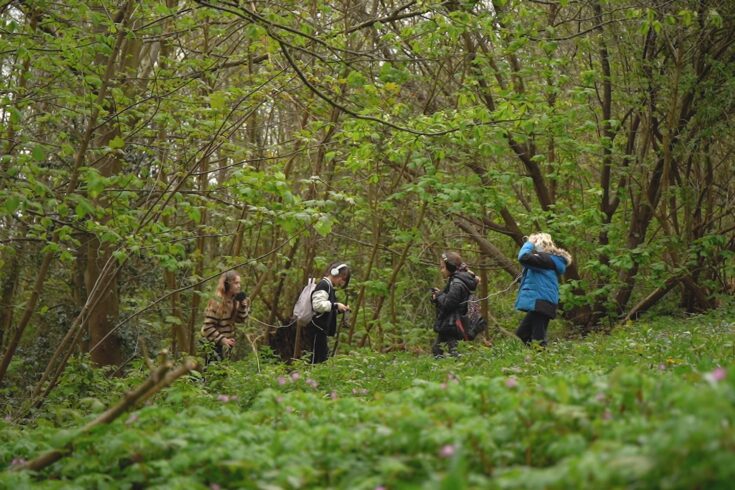 Four children using sound technology while walking in a woodland area.