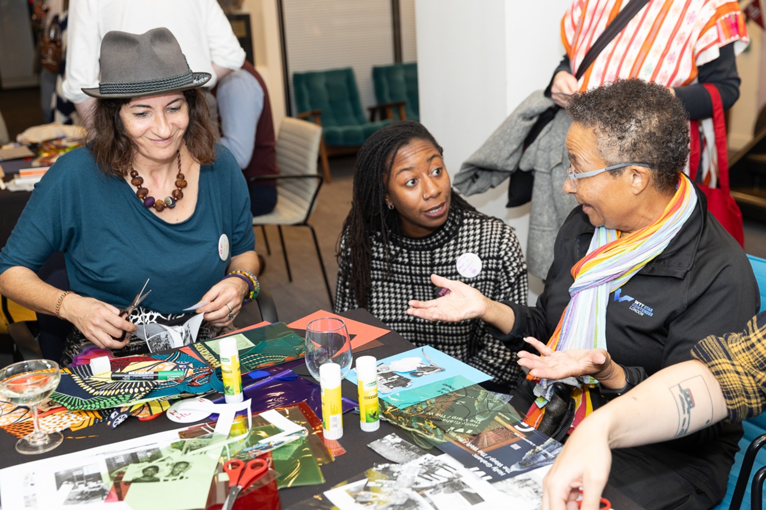 Three people are sitting around a table of crafting materials, two are in conversation and the third person is smiling