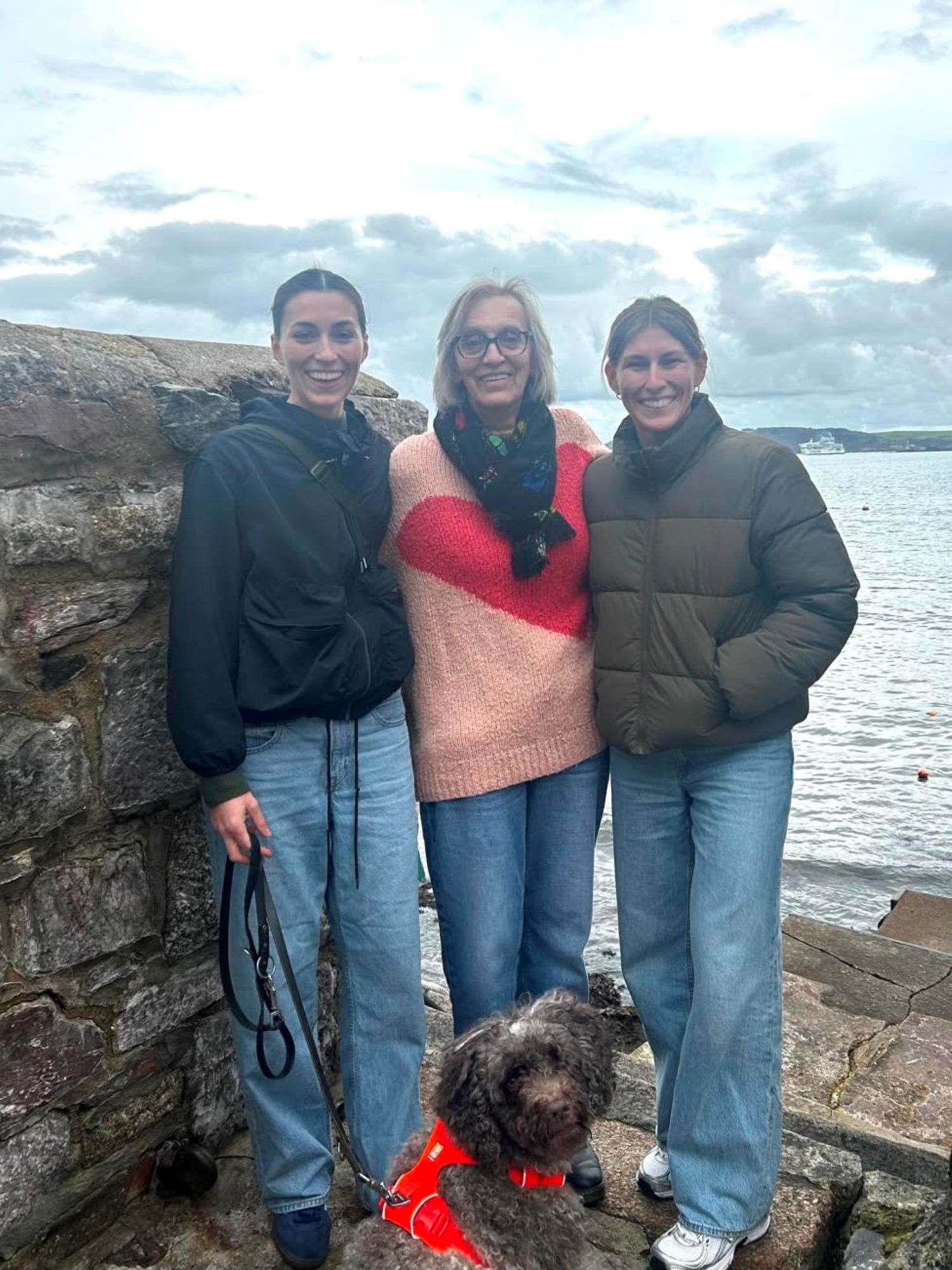 a woman standing with her two daughters and their dog at the beach