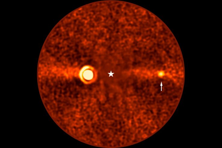 A view through a telescope, showing an orange background with two small orange circles visible. An arrow points at the smallest and faintest circle.