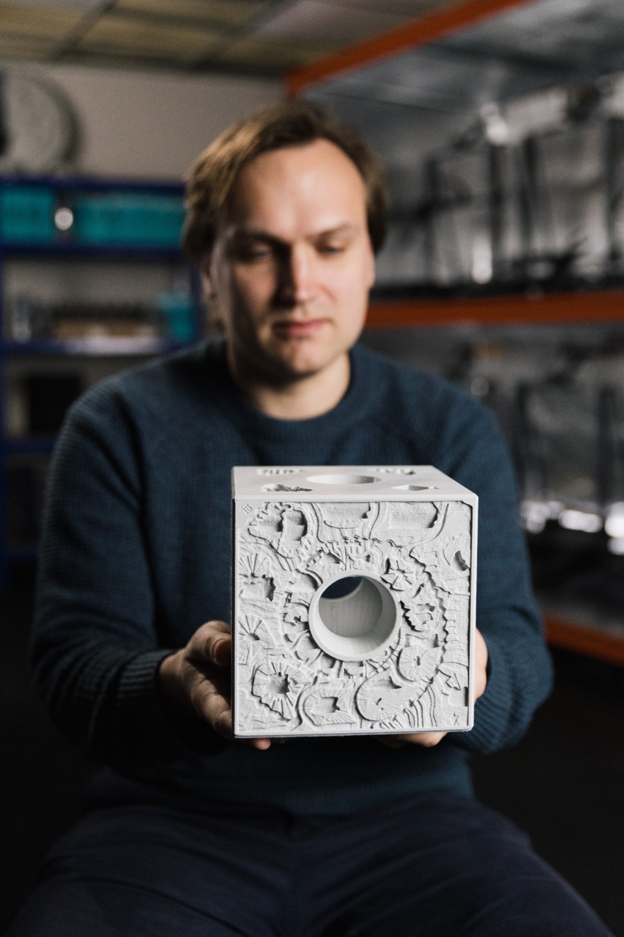 A photo of a man holding a grey cube.